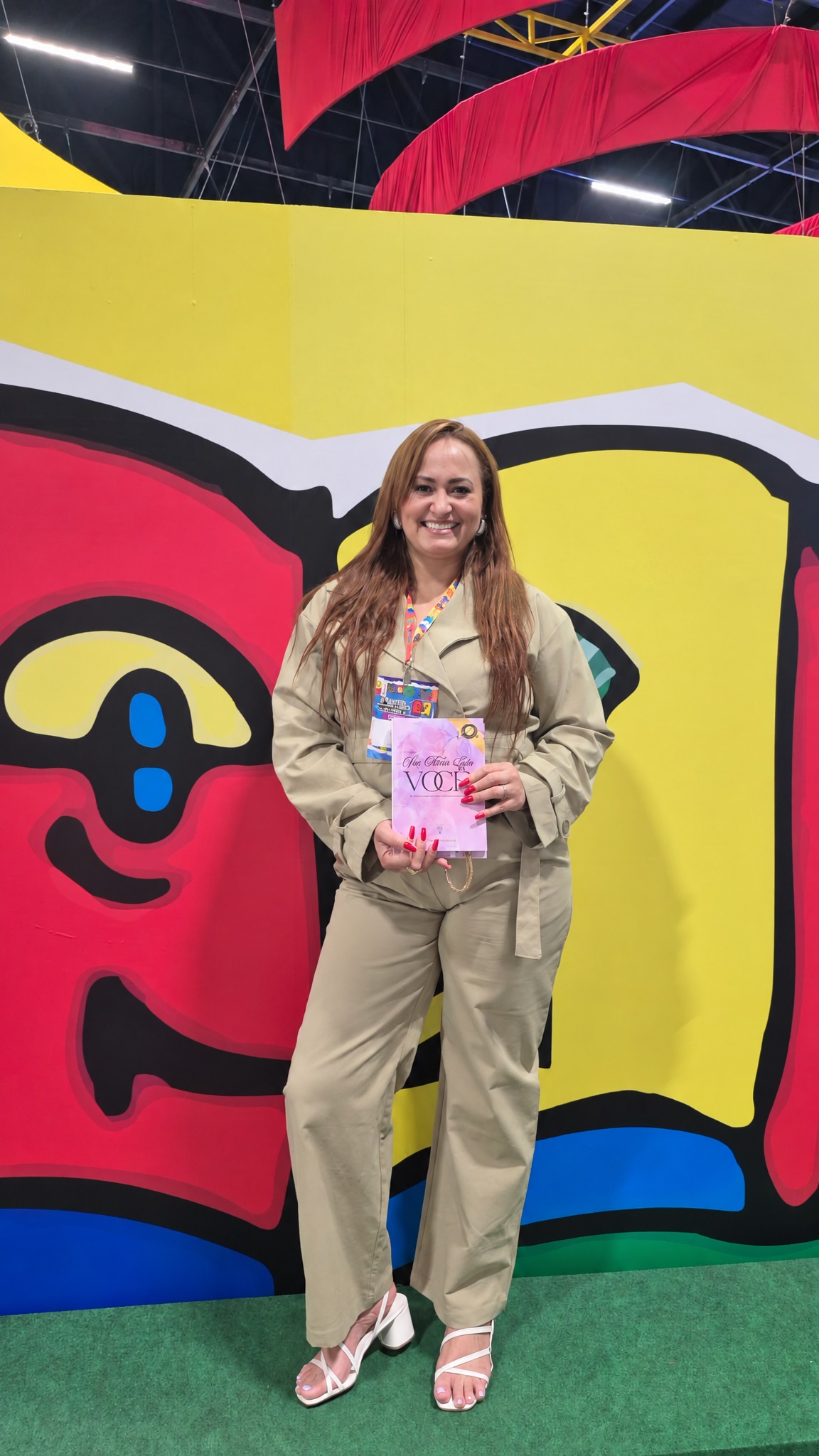 Autora segurando o livro no cenário do livro gigante colorido