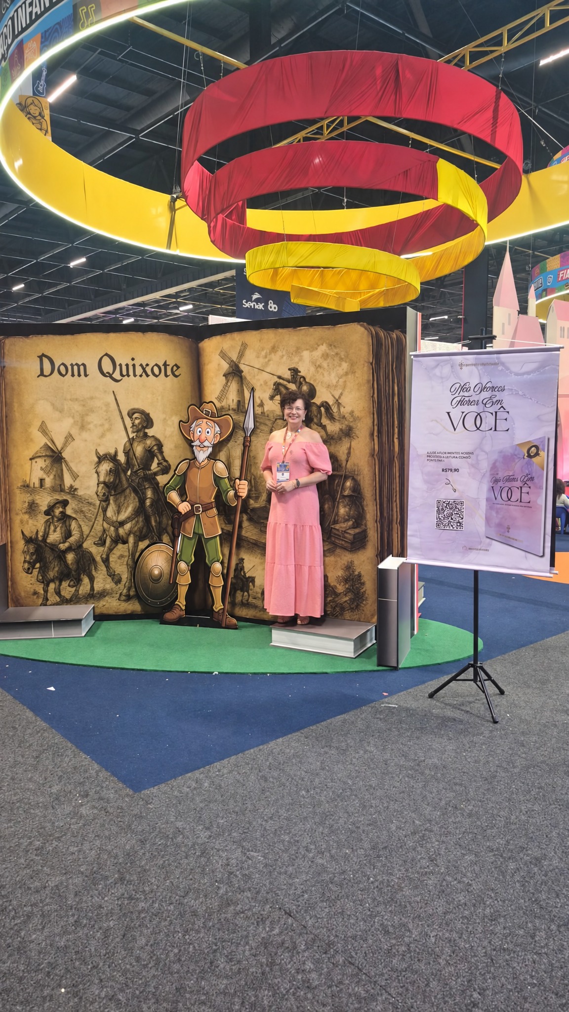 Três autoras com banner do livro no espaço aberto da Bienal