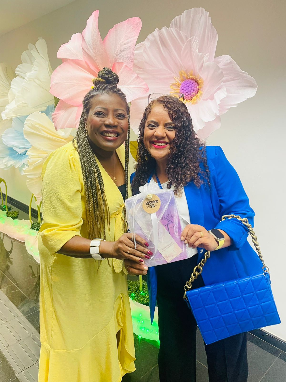 Duas mulheres com bolsa azul em frente às flores