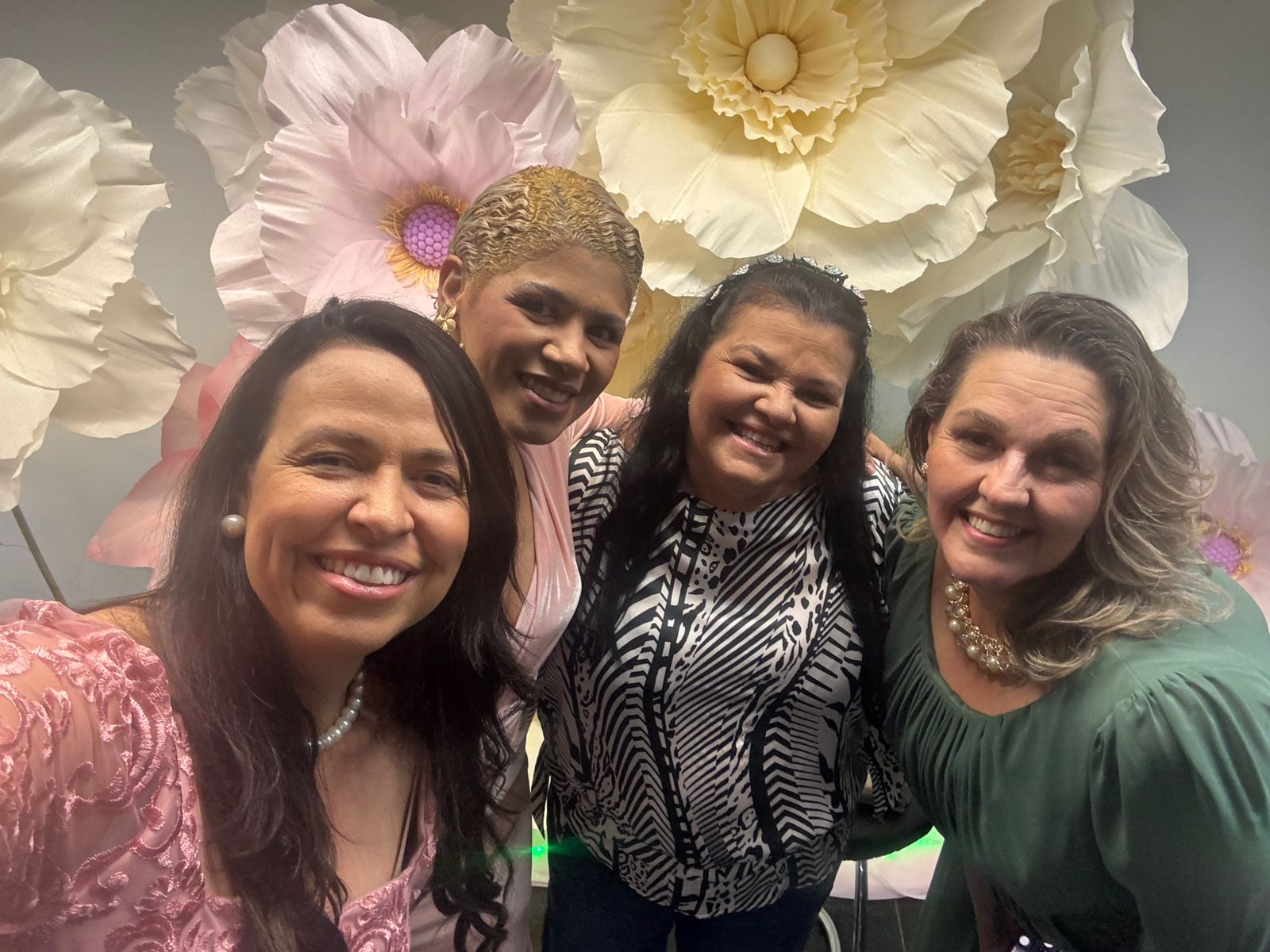 Quatro mulheres sorrindo juntas no painel de flores